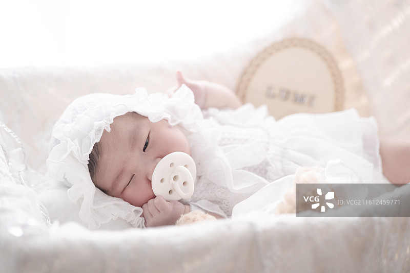 睡在摇篮里嘴咬奶嘴的新生女婴图片素材