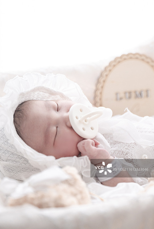 睡在摇篮里嘴咬奶嘴的新生女婴图片素材