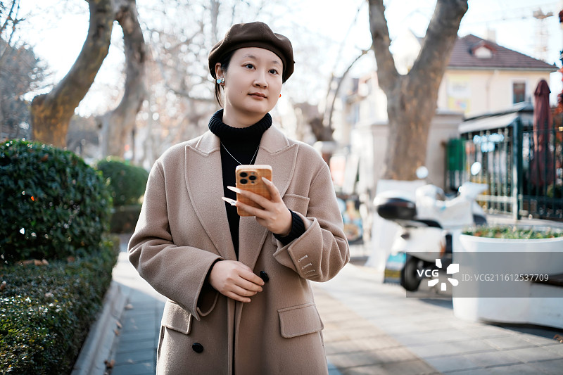 穿着米色外套的年轻女子在户外拿着智能手机图片素材