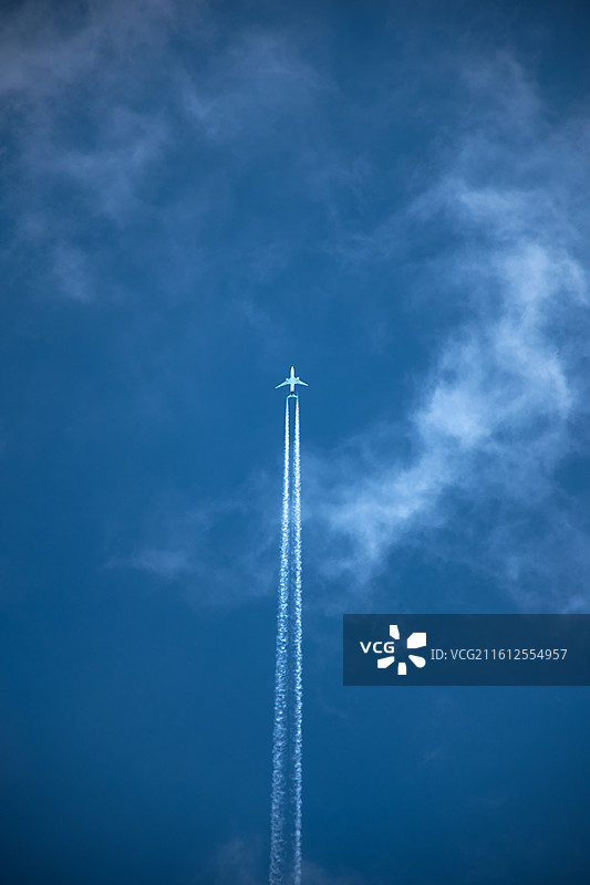蓝天背景下仰拍飞机飞行时的白色水汽尾迹图片素材