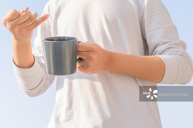 户外蓝天背景下脑瘫患者手持水杯补充水分，展示残障人士的生活自理能力与康复细节。图片素材