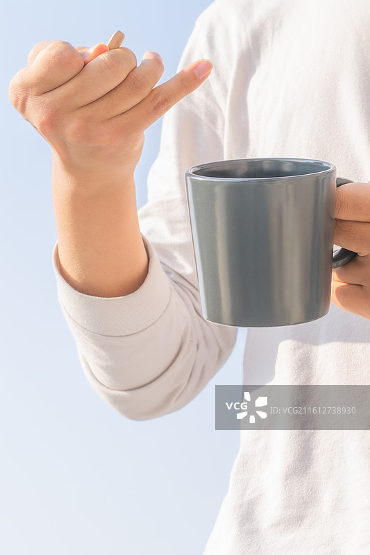 户外蓝天背景下脑瘫患者手持水杯补充水分，展示残障人士的生活自理能力与康复细节。图片素材