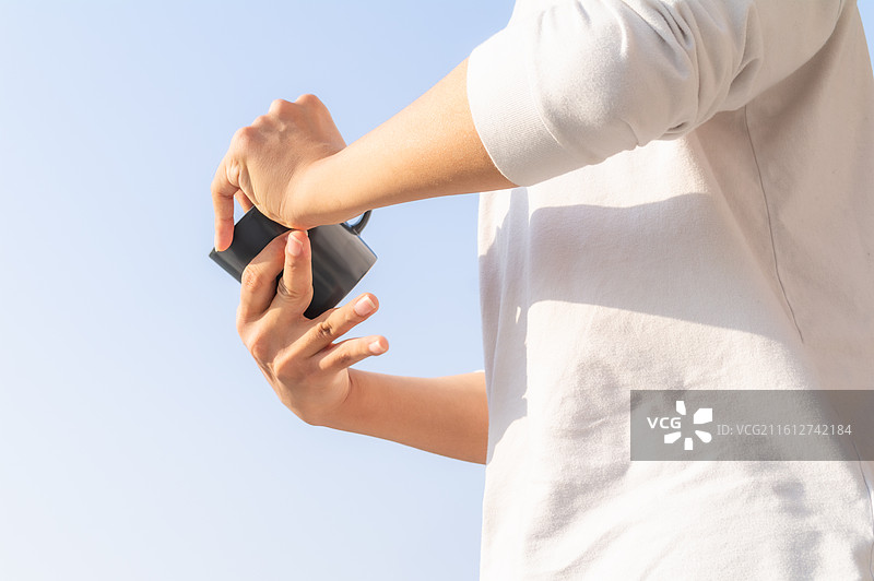 户外蓝天背景下脑瘫患者手持水杯补充水分，展示残障人士的生活自理能力与康复细节。图片素材