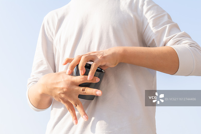 户外蓝天背景下脑瘫患者手持水杯补充水分，展示残障人士的生活自理能力与康复细节。图片素材