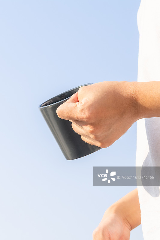 户外蓝天背景下脑瘫患者手持水杯补充水分，展示残障人士的生活自理能力与康复细节。图片素材