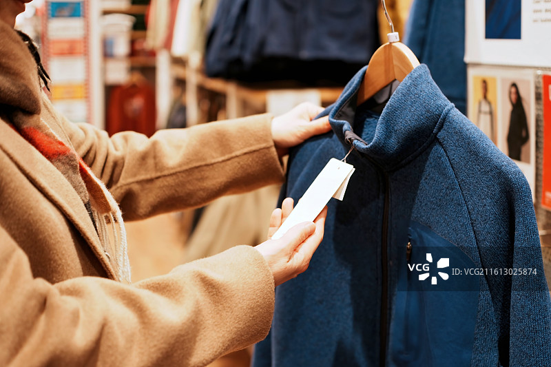 在商店里女人检查蓝色夹克价格标签图片素材