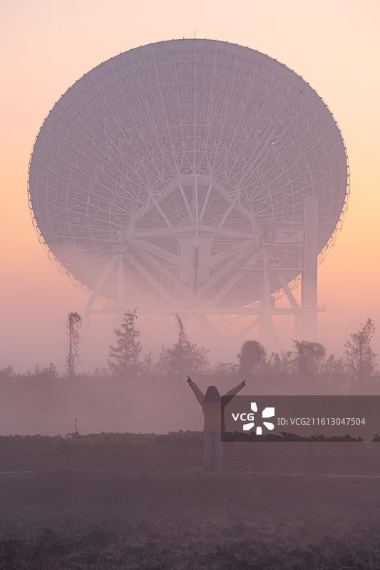 日出晨雾中的天马射电天文望远镜和展开双臂的人图片素材