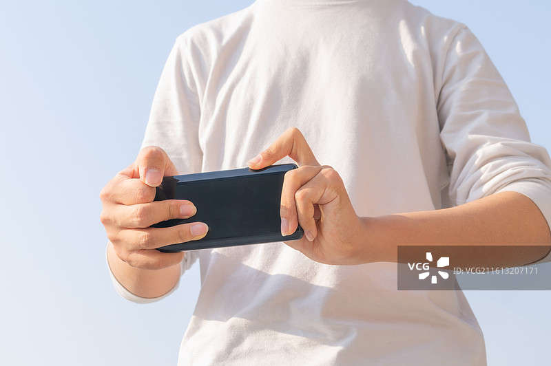 户外蓝天背景下脑瘫患者使用智能手机进行数字化通讯，展示肢体障碍人士的科技无障碍生活。图片素材