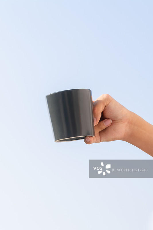 户外蓝天背景下脑瘫患者手持水杯补充水分，展示残障人士的生活自理能力与康复细节。图片素材