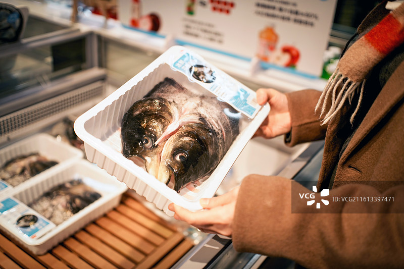 超市里拿着包装好的鱼头的人图片素材