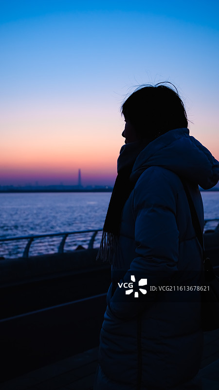 海边日落时分，蓝橙调天空，女人剪影，远处城市天际线图片素材
