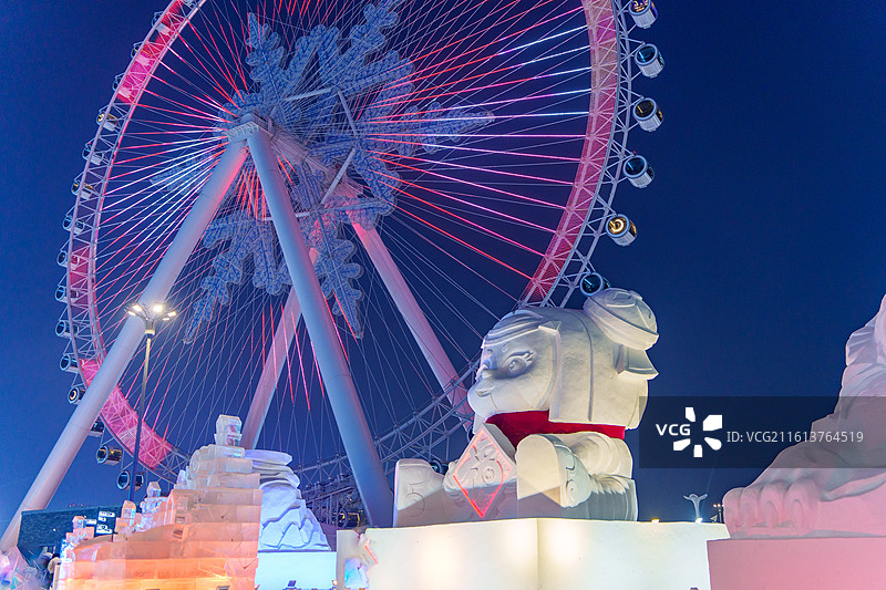 东北黑龙江哈尔滨冰雪大世界夜，粉红灯雪花摩天轮配雪雕，冰雕暖光衬墨蓝天图片素材