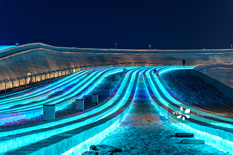 东北黑龙江哈尔滨冰雪大世界的夜晚，超级冰滑梯蓝灯带如银河赛道，蜿蜒冰道超具视觉冲击图片素材