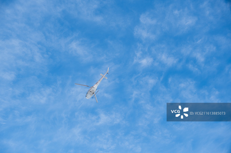 冬天新疆阿勒泰将军山滑雪场的蓝天下直升飞机在空中飞行的低角度视图图片素材