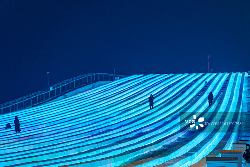 东北黑龙江哈尔滨冰雪大世界夜晚，并制作的超级大滑梯如星河滑道，人影穿梭添动感图片素材