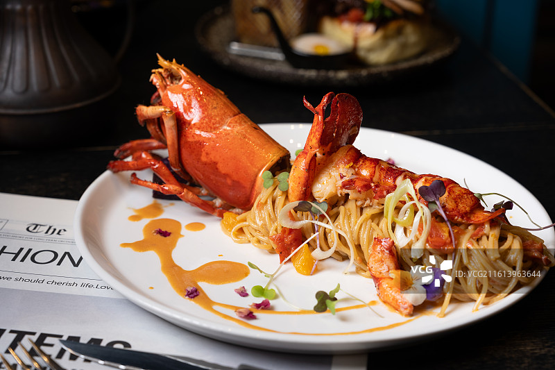 白碗盛装的整只波士顿龙虾意粉，搭配樱桃番茄、微型蔬菜并淋上浓郁海鲜酱汁。图片素材
