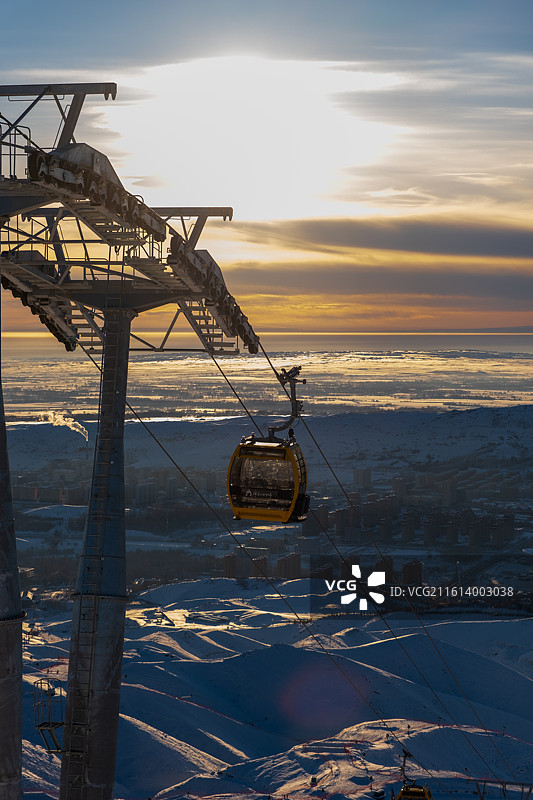 冬天新疆阿勒泰将军山滑雪场俯瞰冬季雪后雪山与城市景观的高角度俯瞰图，日落时缆车与白雪皑皑的群山景色图片素材