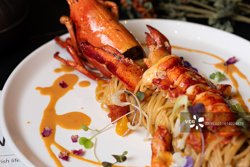 白碗盛装的整只波士顿龙虾意粉，搭配樱桃番茄、微型蔬菜并淋上浓郁海鲜酱汁。图片素材