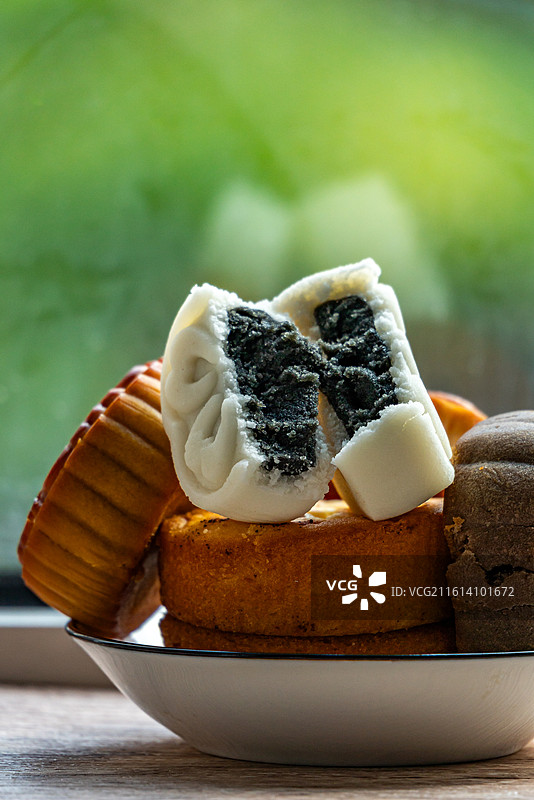 绿色虚化背景中的盘子里的中国中秋节传统美食小吃冰皮糕点月饼甜食特写镜头图片素材