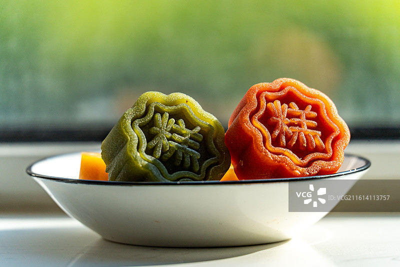 绿色虚化背景中桌子上盘子里的冰皮蛋糕甜食月饼特写镜头图片素材