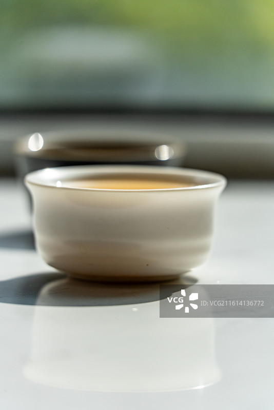绿色虚化背景中窗户阳台上的茶杯茶具一杯清茶特写镜头图片素材