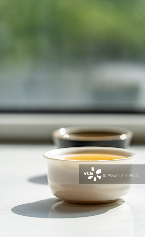 绿色虚化背景中窗户阳台上的茶杯茶具一杯清茶特写镜头图片素材
