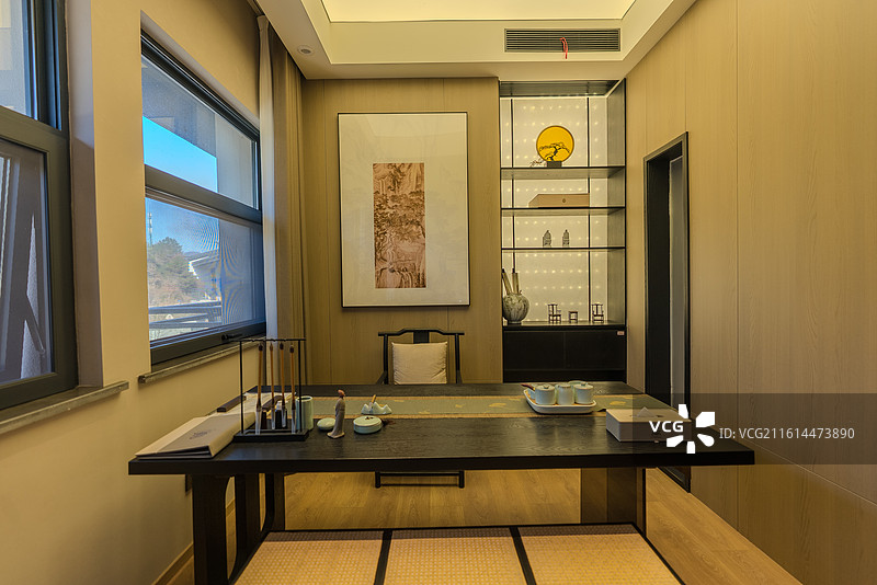 中式茶室摆有一张长方形茶面及椅子桌面摆放茶具和书法笔墨墙面悬挂一幅水墨画右侧设有展示柜左侧是窗户图片素材