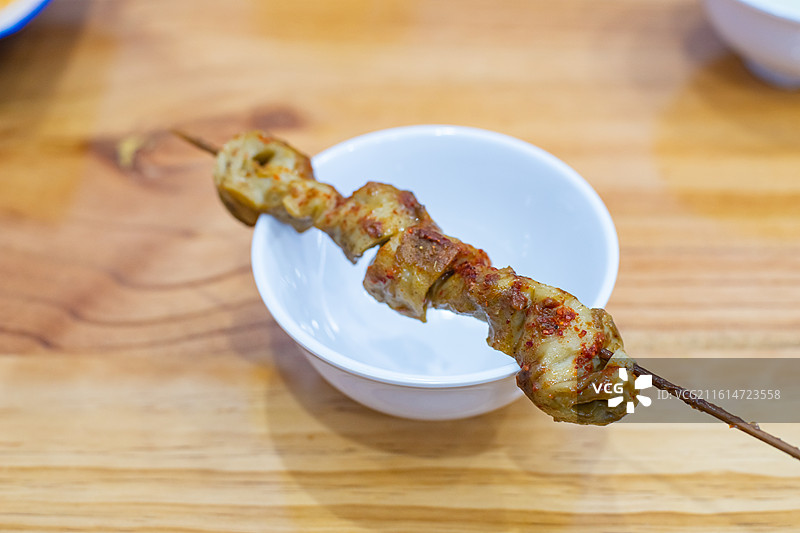 中国饮食产业拍摄主题，瓷碗里放着一支金黄色刷着酱料的烤面筋零食小吃美食，室内无人图像摄影图片素材