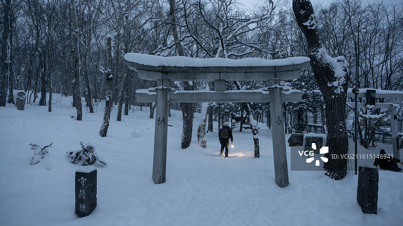 冬季暴雪中，日本北海道小樽天狗山神社鸟居前，一名行人踏雪前行，呈现真实的雪中出行场景。图片素材