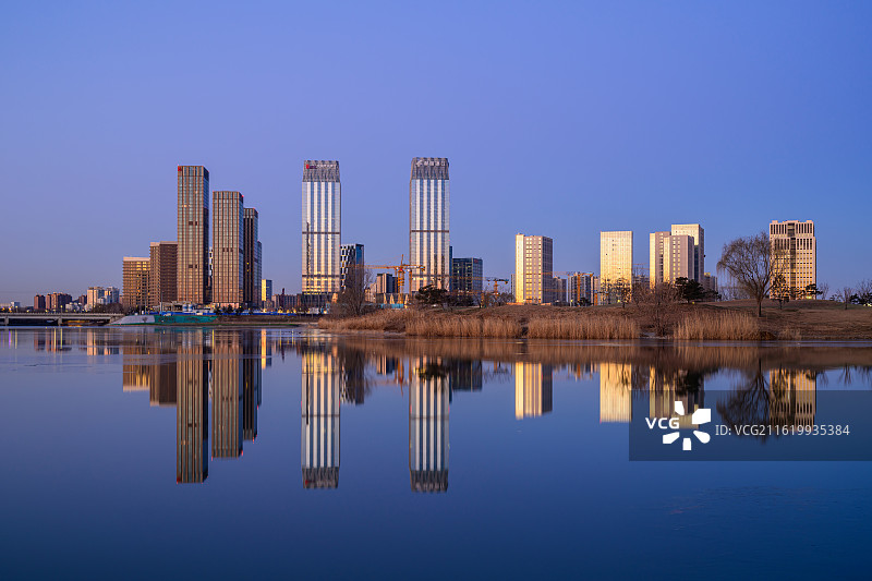 北京通州，冬季清晨，运河商务区天际线倒映在河面，摩天大楼的玻璃幕墙映出霞光。图片素材