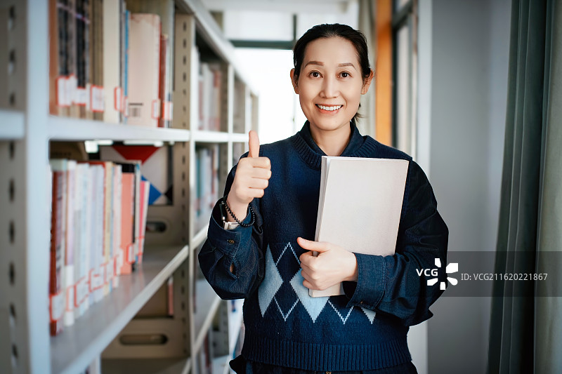 图书馆里拿着书的微笑女人竖起大拇指图片素材