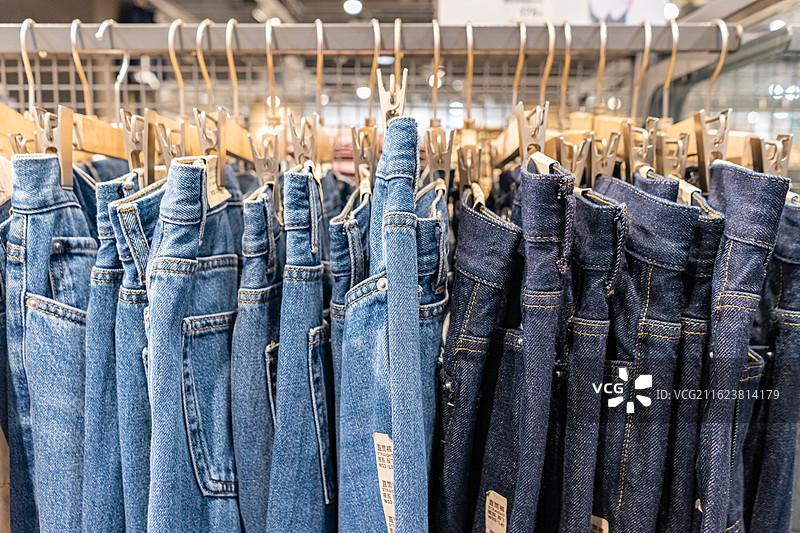 中国商场服装店的生活用品拍摄主题，货架上悬挂的蓝色整齐的牛仔裤休闲裤服装，室内无人图像摄影图片素材