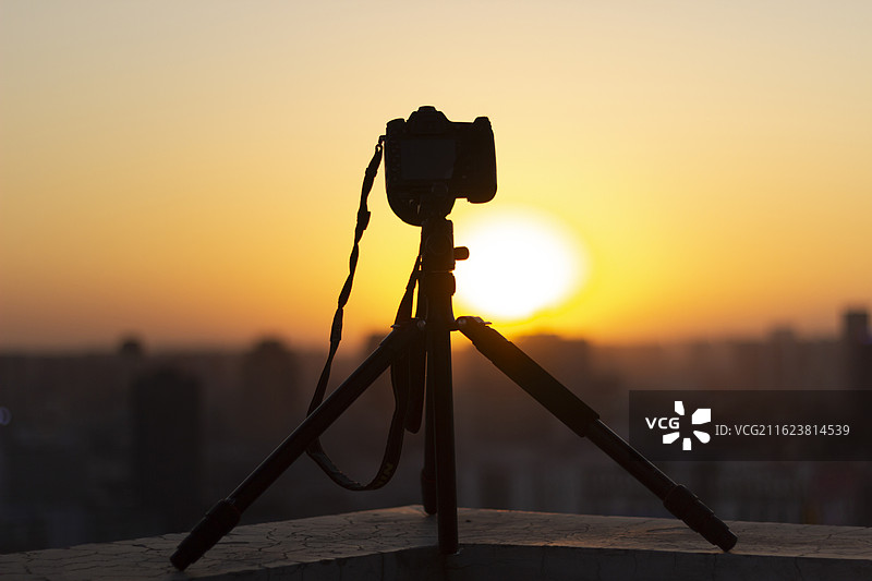三脚架上的相机在日落时分拍摄城市剪影图片素材