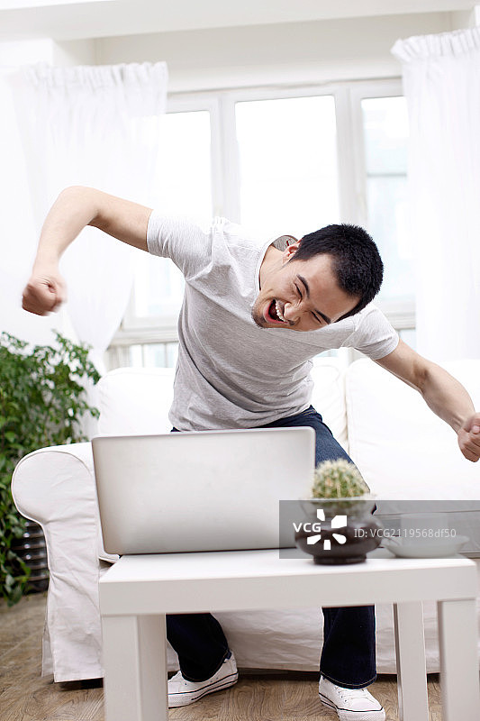 一个坐在白色沙发上用笔记本电脑的青年男士图片素材
