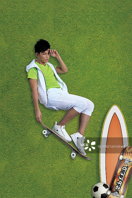躺在草皮上玩滑板的年轻男生图片素材