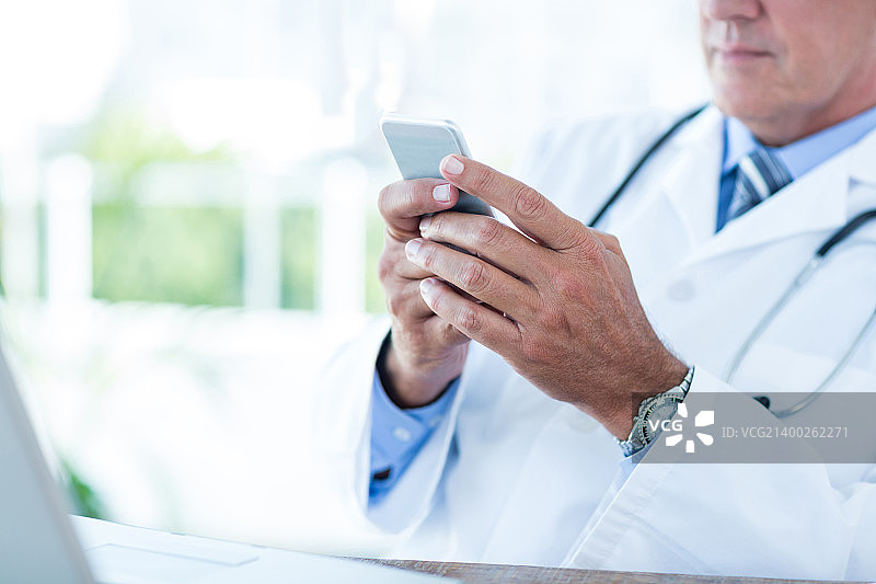 医生在办公室的办公桌旁发短信图片素材