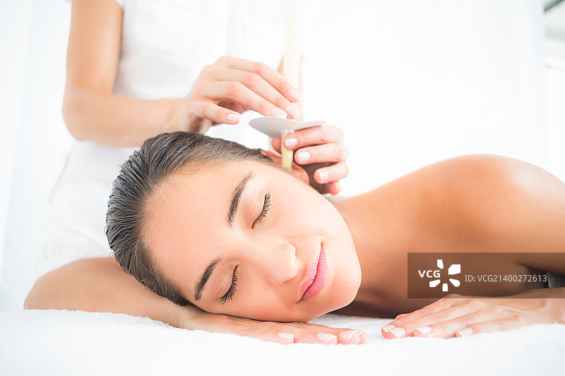 年轻女子在水疗中心接受耳烛护理的侧面照图片素材