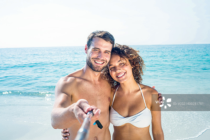 快乐情侣在海滩用自拍杆自拍图片素材