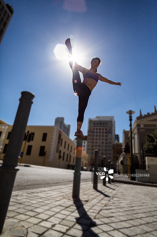 在城市中，运动型女人在系缆柱上保持平衡并抬起腿图片素材