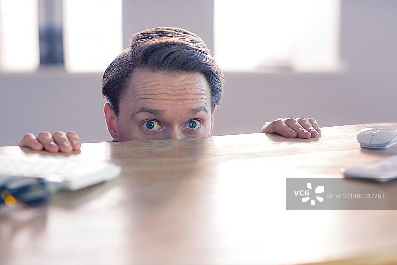 办公室里在办公桌上窥视的紧张商人图片素材