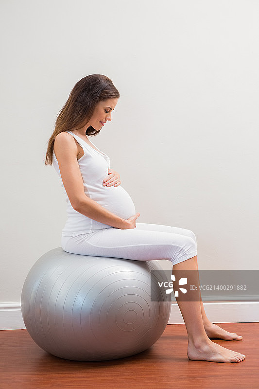 快乐的孕妇坐在房间里的健身球上图片素材