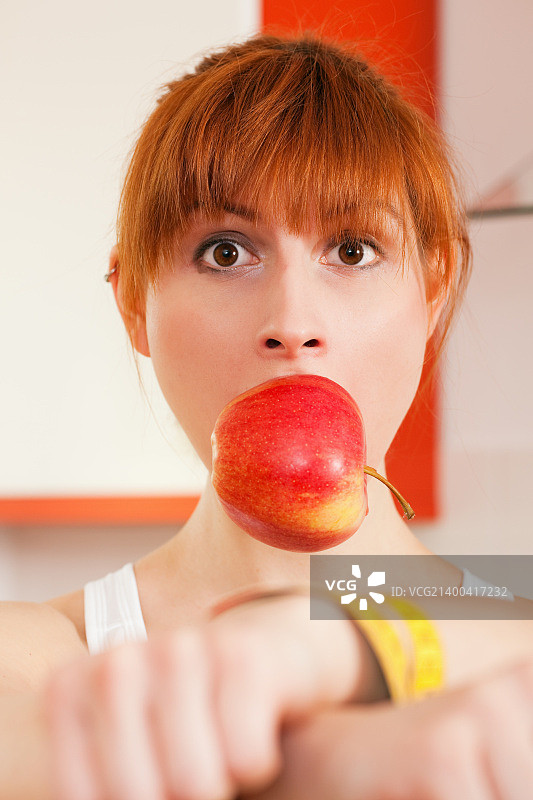 女人被卷尺铐住双手，嘴里塞着苹果，象征饮食失调图片素材
