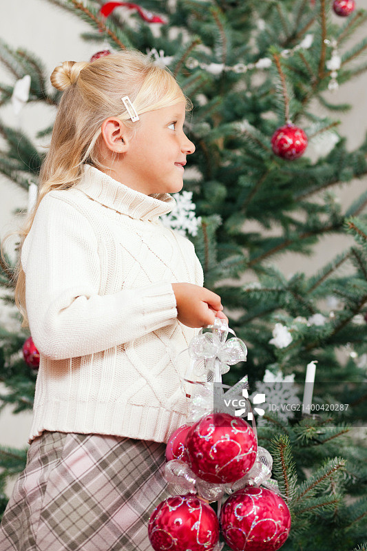 年轻女孩帮忙装饰圣诞树，手拿圣诞球图片素材