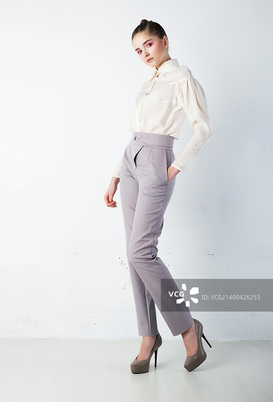 身穿白衬衫和蓝色裤子的年轻漂亮黑发女子在工作室，时尚风格图片素材