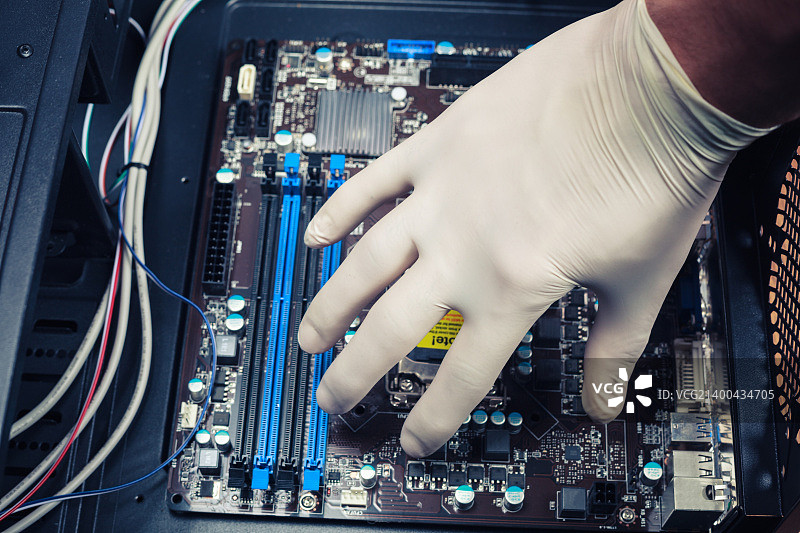 戴橡胶手套的手正在安装电脑组件。图片素材