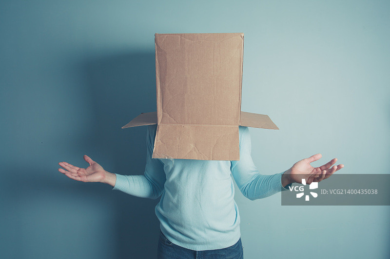 一个困惑的男人头上顶着一个纸箱站着图片素材