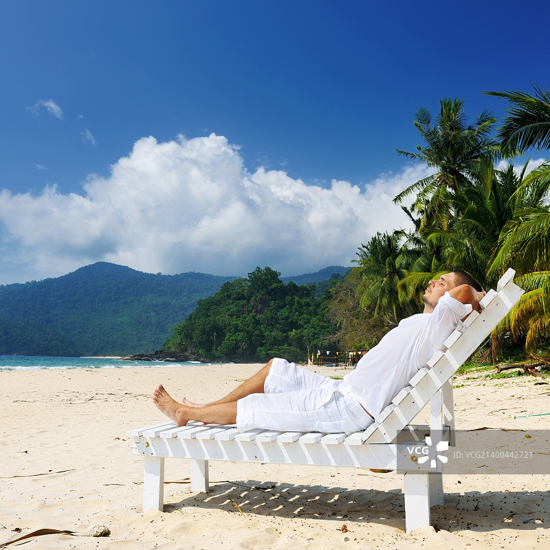 身穿白色衣服的男子在热带海滩上放松图片素材