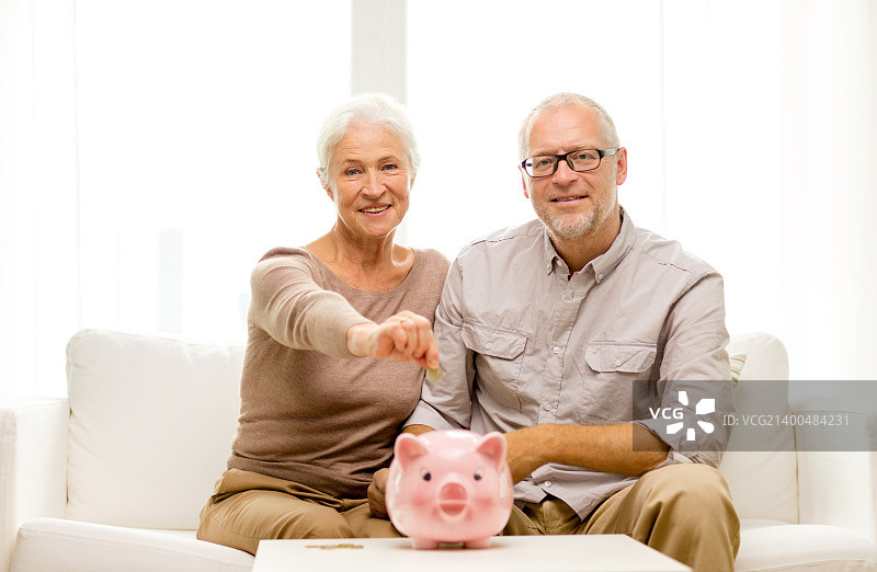 家庭储蓄概念：微笑的老年夫妇在家中展示金钱和存钱罐图片素材