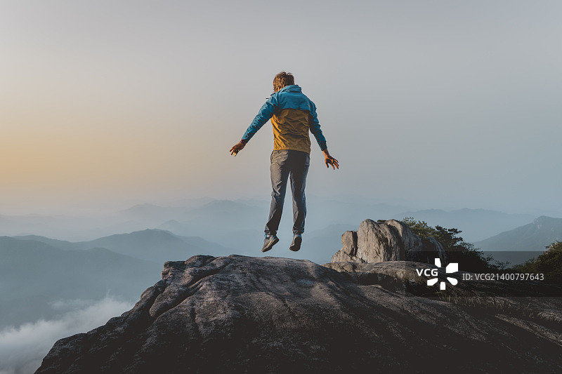 日落时分，男子在高山岩石上跳跃图片素材