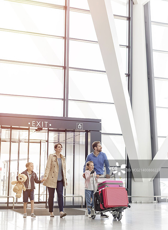 一家人抵达机场，在候机大厅里推着行李车图片素材
